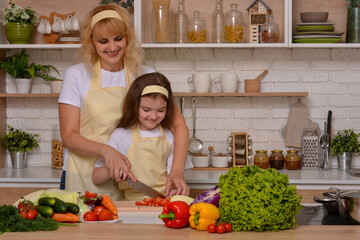 Happy mom teaches daughter to cook (cut vegetables with a knife) at home on the background of the kitchen. Happy pastime, upbringing. Healthy food