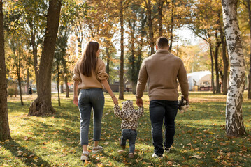 Dad and mom are holding their daughter's hand in the autumn forest. Happy Autumn