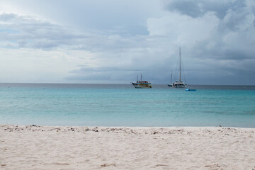 A view from a beach on the west coast of Barbados. There is white sand and blue water with a few...