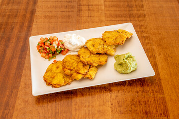 Ripe plantain patacon with dip sauces, guacamole, pico de gallo and cream cheese on wooden table