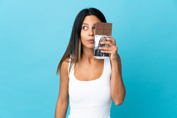 Caucasian girl isolated on blue background taking a chocolate tablet and surprised