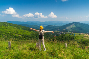 Traveler with a backpack stands with outstretched arms in the mountains in summer. The top of the mountain evokes a good or elated mood