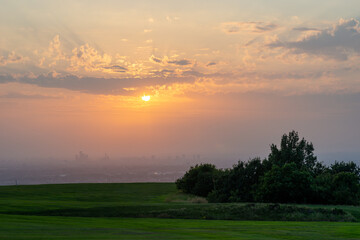 Sun setting over Manchester city on a dusty summer evening. The poor air quality and clouds helped produce a spectacular deep orange red sunset with sun rays. England, UK