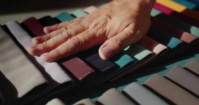 A man's hand touches samples of multi-colored fabric. Designer selects textiles for the project