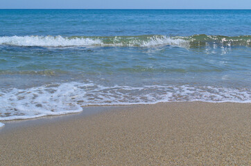 Summer background. Blue sea wave with foam on the sandy shore.