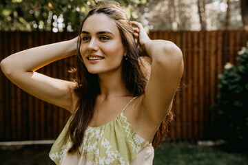 Portrait of a young brunette woman, adjusting her hair, outdoors, smiling.