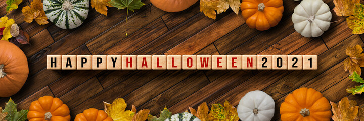 cubes with message HALLOWEEN 2021 framed by pumpkins on wooden background