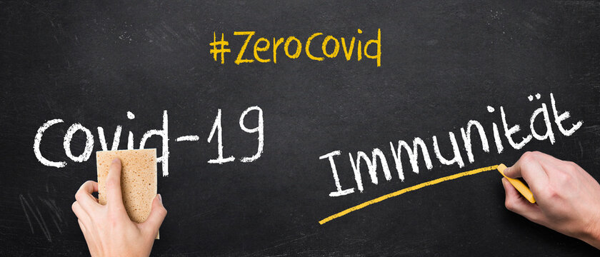 hand writing the German message #ZEROCOVID COVID-19 IMMUNITY on a blackboard