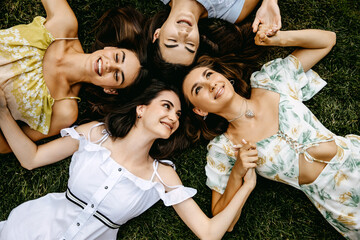 Four young women lying on grass, laughing, top view.
