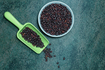 black beans in a ceramic bowl and a plastic spoon on a dark marble surface