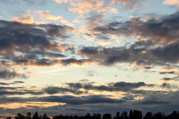 Blue sky with large dark cumulus clouds illuminated by the evening setting sun as a natural background
