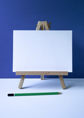 wooden easel with white board with space for text, blue background, green pencil.