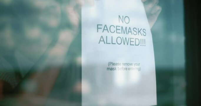 Woman places an anti-mask sign on door.