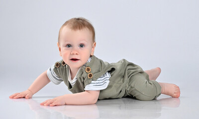 Naklejka premium little boy in a green casual overalls, barefoot, lies on the floor and looks with interest into the frame. The kid stopped frozen crawling on the floor