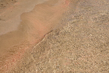 Clear waves and colorful sand on tropical sandy beach in Crete Greece.