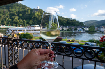 Hand holding glass of white quality riesling wine served on outdoor terrace in Mosel wine region...