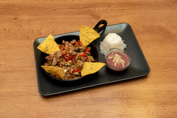 Mexican beef wire stew with peppers and meat with cheese, corn chips and rice with dip sauce on black tray