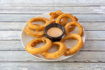 Ration of onion rings battered in American style with sauce to dip in the center