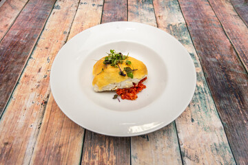 Great recipe for cod gratin with cheese, dehydrated red pepper and vegetable sprouts on top on a white plate