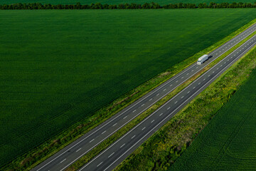 white truck on the higthway among the green fields with goods. cargo delivery driving on asphalt road  seen from the air. Aerial view landscape. drone photography.