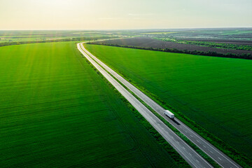 alone white truck on the higthway at sunset. cargo delivery driving on asphalt road among the green fields with goods. seen from the air. Aerial view landscape. drone photography.