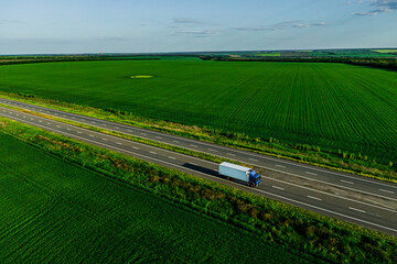 one blue truck  on the higthway at sunset among the green fields with goods cargo delivery. seen from the air. Aerial view landscape. drone photography.