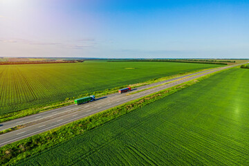 red and green trucks on the higthway at sunset driving on asphalt road among the green fields. seen from the air. Aerial view landscape. drone photography. convoys with cargo Left side traffic