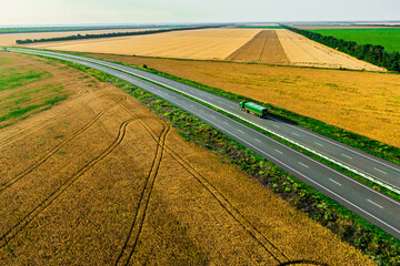 green truck on the higthway among the wheat fields. cargo delivery driving on asphalt road  seen...
