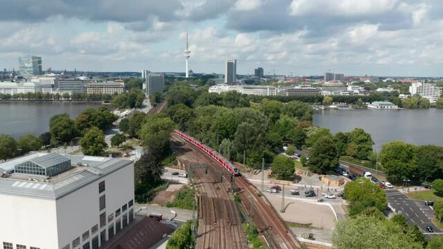 Aerial view of train unit driving on multi-track railway line leading through city. Pleasant environment with trees and water area. Free and Hanseatic City of Hamburg, Germany