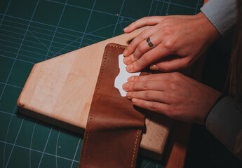 Top view of two hands pressing a white sticker on a brown leather wallet on a wooden surface