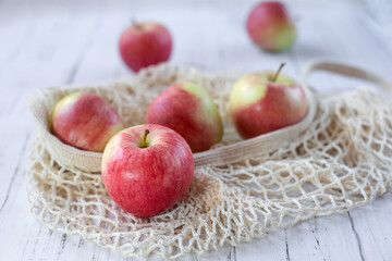 Ripe delicious red apples in a mesh bag on a light wooden background. New summer harvest. The concept of healthy food.