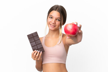 Little caucasian girl isolated on white background taking a chocolate tablet in one hand and an...