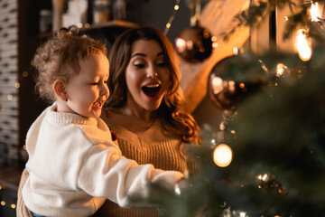 Merry Christmas and Happy Holidays. The mother held her daughter near the tree and decorated the tree indoors. morning before Christmas. Close-up portrait of a loving family