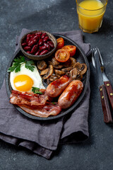 English breakfast with fried eggs, bacon, sausages, beans, toasts on black background