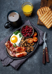 English breakfast with fried eggs, bacon, sausages, beans, toasts on black background