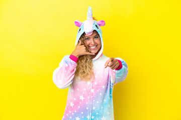 Girl with curly hair wearing a unicorn pajama isolated on yellow background making phone gesture and pointing front