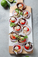 Raw Seafood shellfish scallops with lemon, cilantro and michelada beer drink on white board, gray background