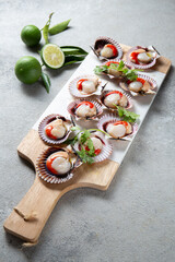 Raw Seafood shellfish scallops with lemon, cilantro and michelada beer drink on white board, gray background