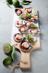 Raw Seafood shellfish scallops with lemon, cilantro and michelada beer drink on white board, gray background