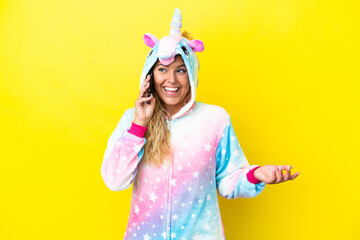 Girl with curly hair wearing a unicorn pajama isolated on yellow background keeping a conversation with the mobile phone with someone