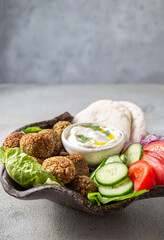 Falafel, fresh vegetables and pita bread on clay plate, gray background