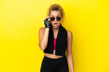 Sport woman with towel isolated on yellow background with glasses and surprised