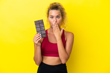 Girl with curly hair isolated on yellow background taking a chocolate tablet and surprised