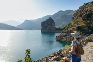 Woman with hat and a small backpack admiring the landscape of the beautiful Caniles reservoir...