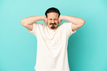 Young caucasian man isolated on blue background frustrated and covering ears