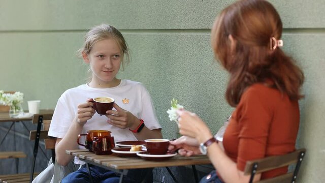 mother and daughter sitting in the street caffee and speaking. Focus on a dughter girl
