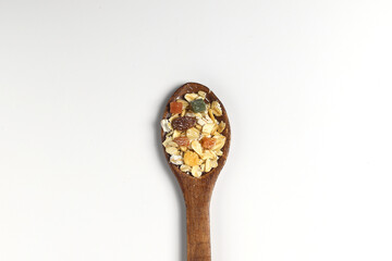Breakfast cereals in wooden spoon. Healthy muesli with oat flakes, nuts and raisins isolated on white background.