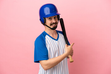 Young caucasian man playing baseball isolated on pink background pointing back