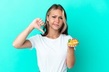 Young Russian woman holding a fruit sweet isolated on blue background showing thumb down with negative expression