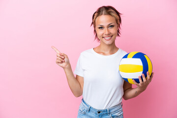 Young Russian woman playing volleyball isolated on pink background pointing finger to the side